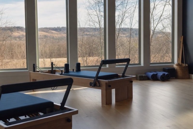 Pilates reformers in a quiet studio, mats rolled up on light floorboards as morning sun comes in