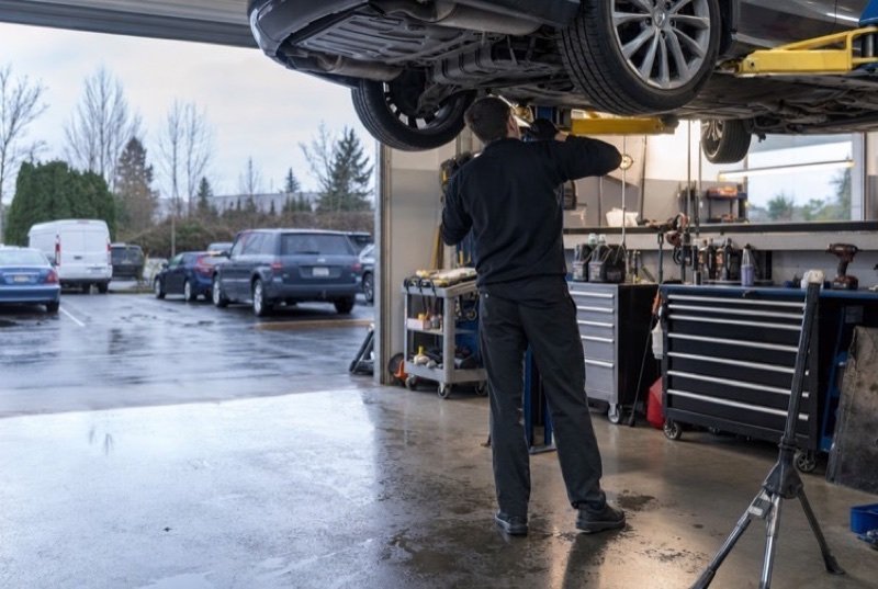 Inside a clean auto shop, a sedan up on the lift while a technician works beneath it, everyday work in the repair industry